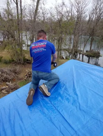 A Tri-County All Restorations technician securing an emergency tarp over a storm-damaged roof